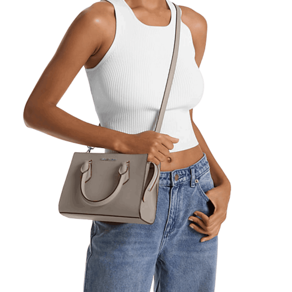 Person wearing a white tank top and blue jeans holding a gray handbag.